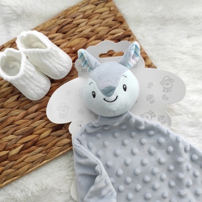 Manta cinza de pelúcia com cabeça de animal e sapatinhos brancos ao lado