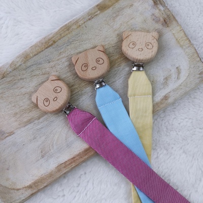 Clipes de chupeta em madeira com rostos de animais e fitas coloridas sobre bandeja de madeira