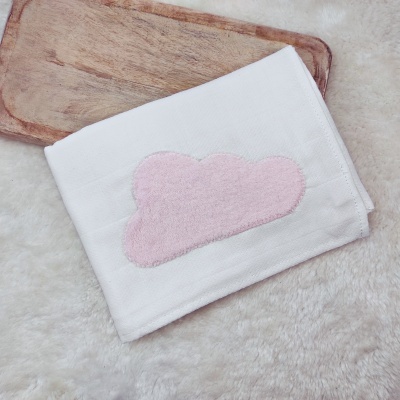 toalha branca com bordado de nuvem rosa sobre fundo felpudo e tábua de madeira