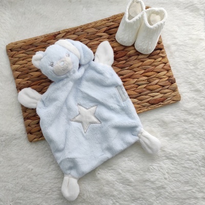 Boneco de peluche azul claro com estrela branca e botins brancos em tapete de fibras naturais