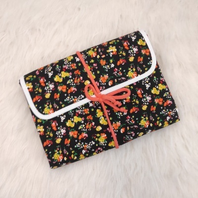 Estojo floral preto com fecho de cordão cor de coral sobre fundo claro peludo