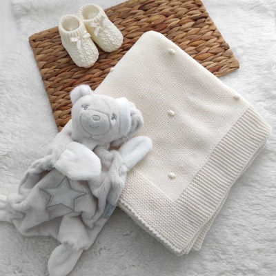 Manta de malha branca, peluche de urso cinzento e camisola branca de bebé