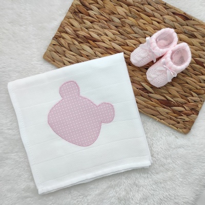 lençol branco com aplique rosa e sapatinhos rosa sobre tapete castanho