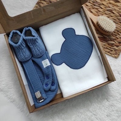 Caixa com botins de malha azuis, suspensório azul e manta branca decorada com cabeça de urso azul