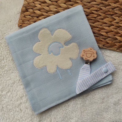 Manta azul clara com aplique de ovelha e fita com prendador de madeira.