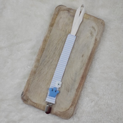 Clipe de chupeta azul e branco sobre tabuleiro de madeira