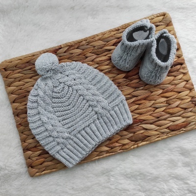 Conjunto de gorro e sapatinhos de bebê cinza tricotados sobre tapete de palha