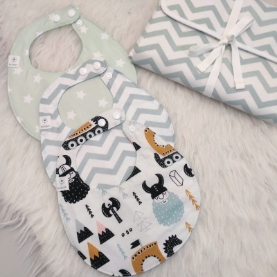 Três babetes para bebé com padrões diferentes sobre superfície peluda e capa dobrada com padrão de ziguezague