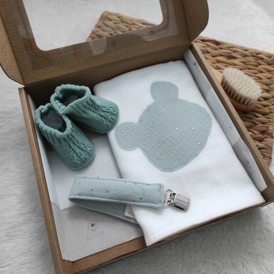 Conjunto de bebé com manta, botinhas e prendedor de chucha azul claro numa caixa de cartão