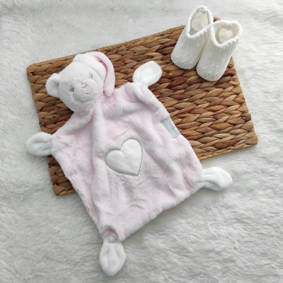 Brinquedo/lencinho de urso cor-de-rosa e branco com coração e botas brancas felpudas sobre tapete de fibras naturais