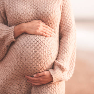 Mulher grávida de suéter bege segurando a barriga