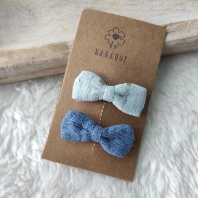 Dois molas de cabelo em forma de laço azul clara e azul escura em cartão castanho com texto e desenho de flor