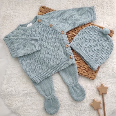 Conjunto de malha azul claro para bebé com casaco, calças e gorro, sobre tapete branco com estrelas em madeira
