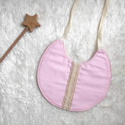 Babete de bebé rosa com renda bege e varinha de madeira com estrela sobre tecido branco felpudo