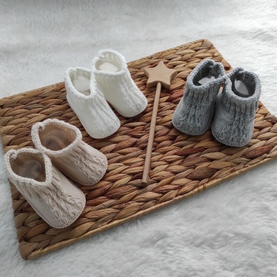 Três pares de sapatinhos de bebé em malha bege, branco e cinza sobre base de palha com estrela decorativa