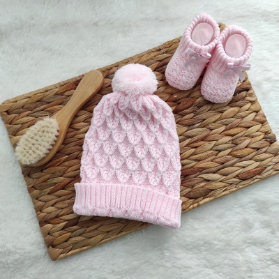 Conjunto rosa de gorro e botins de bebé em malha com escova de cabelo sobre tapete trançado