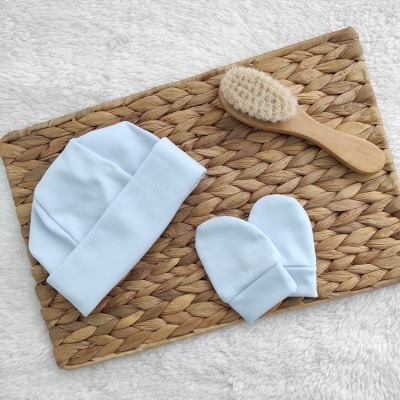 conjunto de gorro e luvas azuis claras para bebé com escova de madeira em tapete de tom castanho entrelaçado