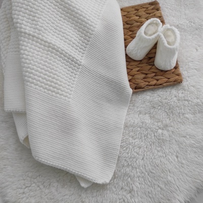 Cobertor branco de malha, meias brancas e base natural sobre superfície felpuda branca