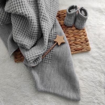 Manta cinzenta e sapatinhos de bebé sobre tapete de fibra natural