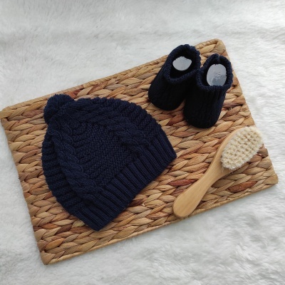 Gorro de malha azul escuro, sapatilhas azuis escuras e escova de cabelo de madeira sobre tapete de ráfia