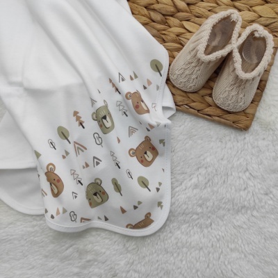 Manta branca com estampado de ursos e árvores e sapatilhas de malha bege à direita