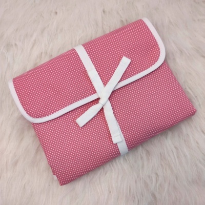 Bolsa rosa com bolinhas brancas e fita branca sobre superfície peluda branca