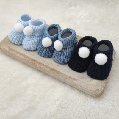 Três pares de sapatinhos de bebé em tricô azul claro, médio e escuro com pompons brancos