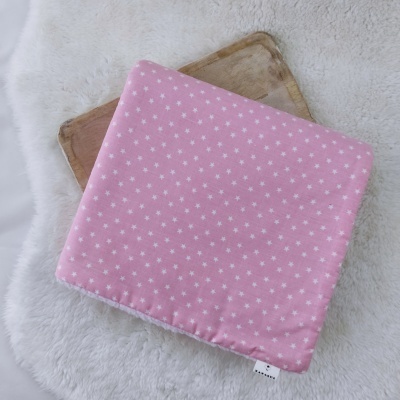 Almofada rosa com estrelas brancas sobre tecido branco felpudo e madeira