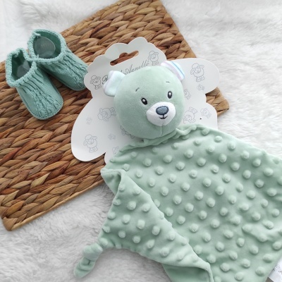 Manta de pelúcia verde claro com rosto de urso e sapatinhos verdes em fundo branco com tapete de palha