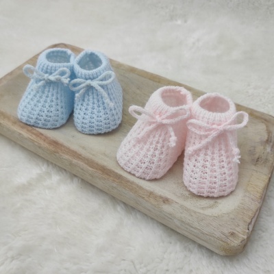 Dois pares de sapatinhos de bebé em crochet, azul e rosa, com laços, sobre tábua de madeira clara