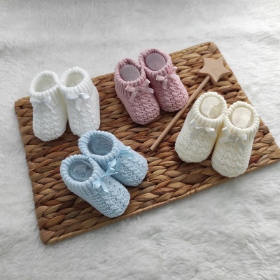 Quatro pares de sapatinhos de bebé tricotados coloridos sobre base de palha branca