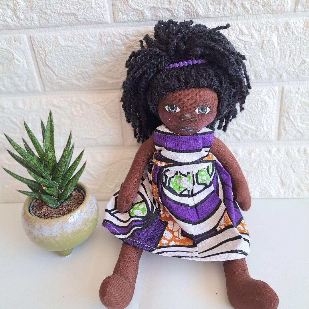 Aisha Boneca de tecido com vestido colorido e planta suculenta ao lado