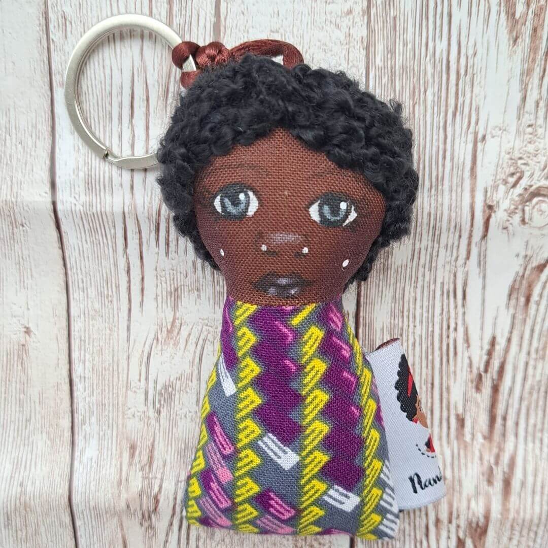Porta-Chaves Boneca - Elegância Afro Chaveiro boneca com cabelo preto e roupa colorida geométrica