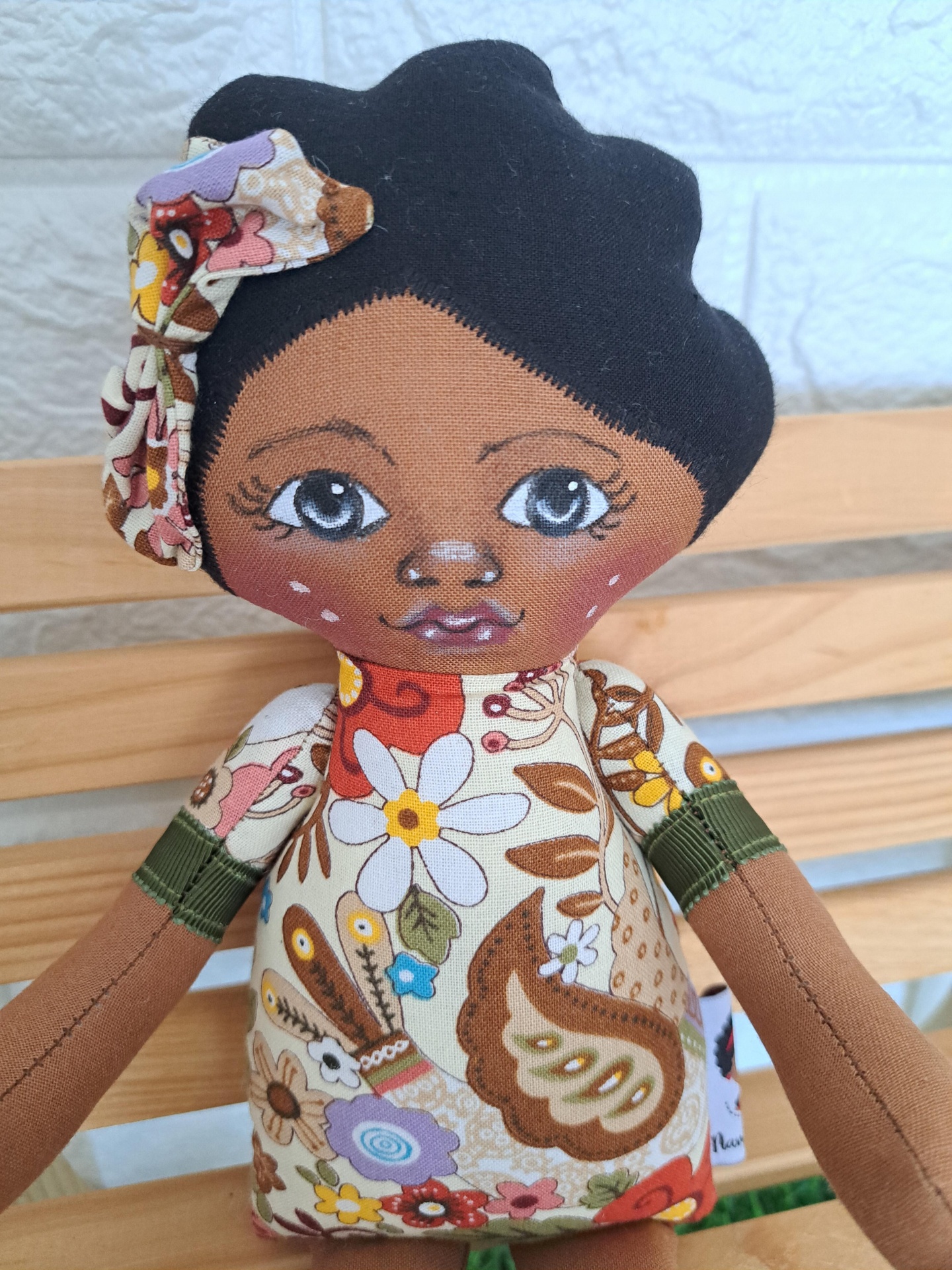 Aminata Boneca de tecido com vestido floral colorido e cabelo preto.