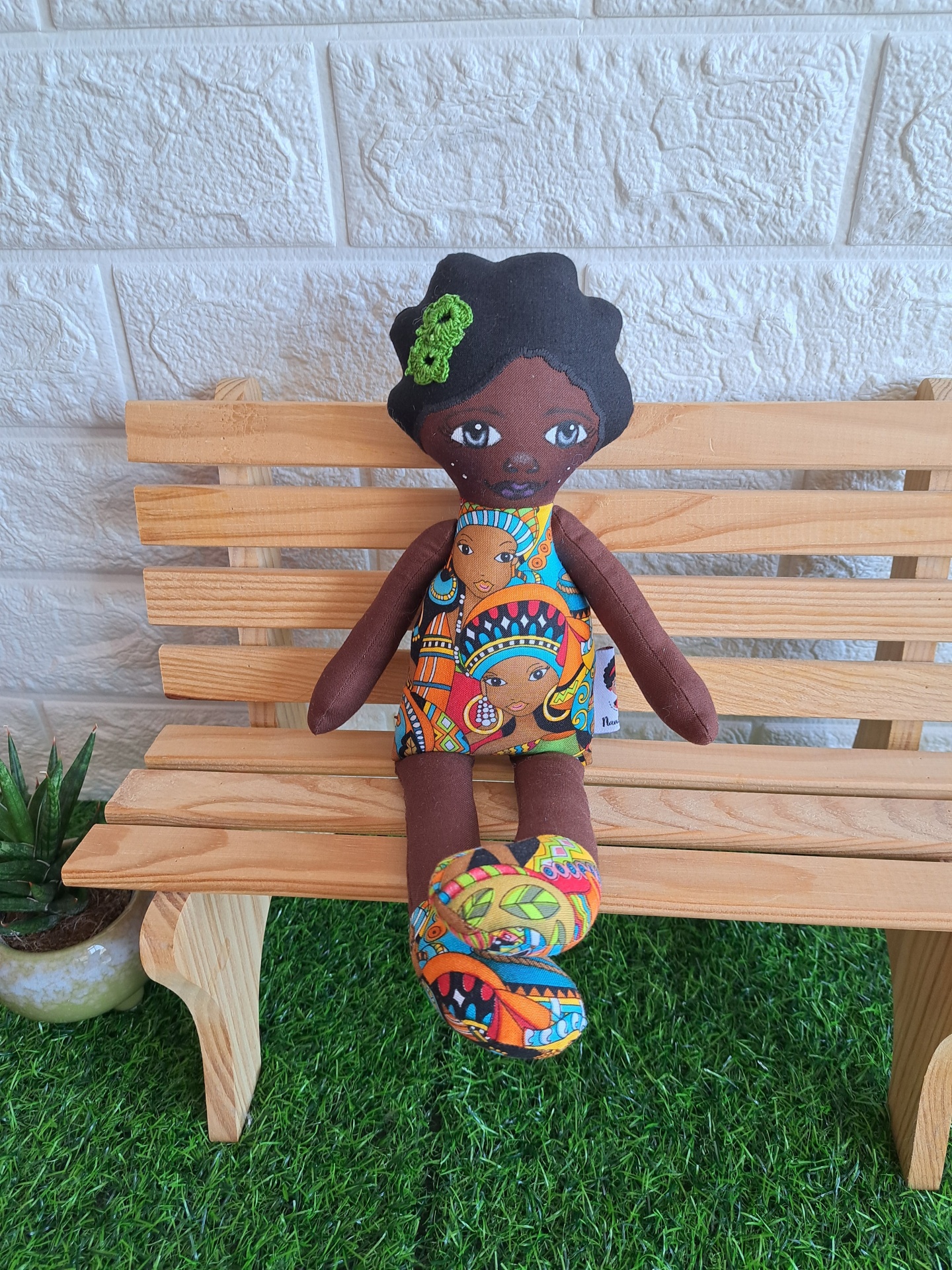Zia Boneca de tecido colorida sentada num banco de madeira