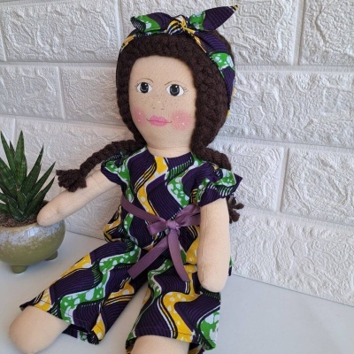 Boneca de tecido com vestido colorido sentada ao lado de uma planta