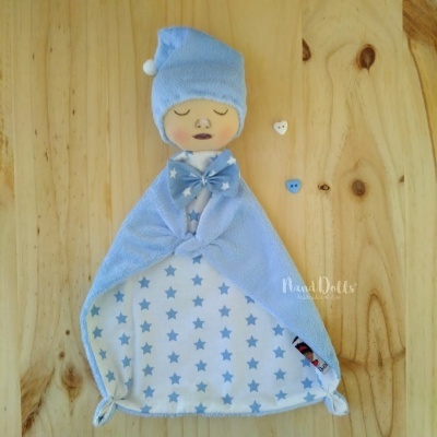 Boneco de bebé com chapéu e manta azul com estrelas, sobre madeira clara