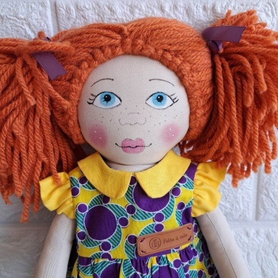Boneca de pano com cabelo laranja, vestido colorido e etiqueta 'Feita à mão'