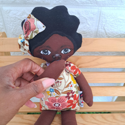 Boneco tecido de pele castanha escura com vestido floral colorido sentado num banco de madeira