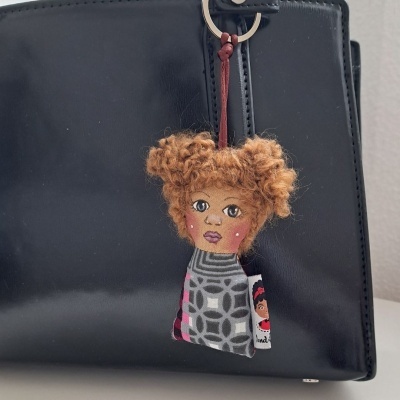 Chaveiro de boneca com cabelo encaracolado castanho claro pendurado numa mala preta