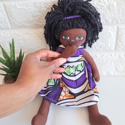 Boneca de pano com vestido colorido e cabelo cacheado ao lado de planta