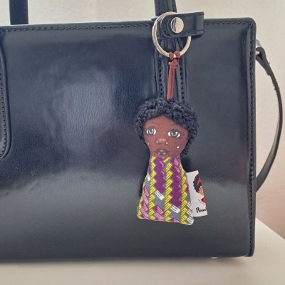 Chaveiro em tecido com rosto bordado e roupa colorida pendurado em mala preta