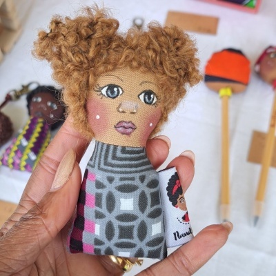 Boneca artesanal em tecido com cabelo encaracolado castanho claro e vestido geométrico cinza