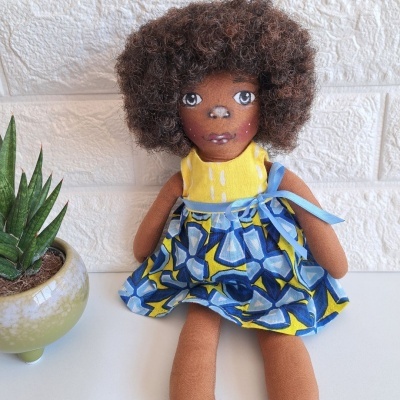 boneca de tecido com vestido azul e amarelo ao lado de planta em vaso