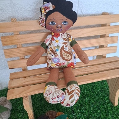 Boneca de pano com vestido floral sentada num banco de madeira