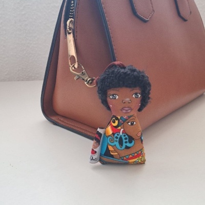 Chaveiro decorativo com boneco em tecido colorido em frente a mala castanha