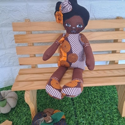 Boneca de tecido africana sentada num banco de madeira com abóbora de tecido.