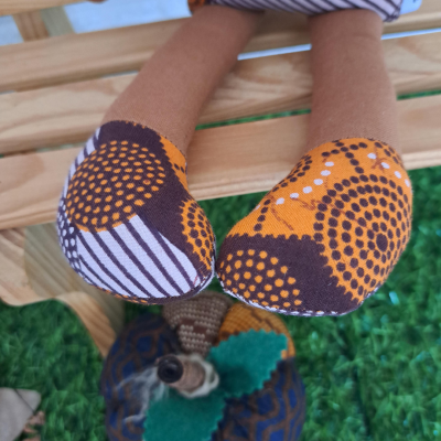 Boneca de tecido com pés em padrão laranja, castanho e branco sentada numa superfície de madeira