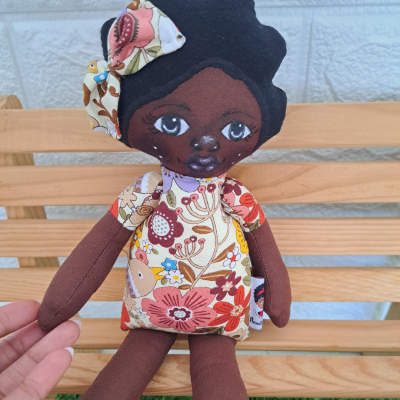 Boneca de tecido castanha com vestido floral sentado em banco de madeira