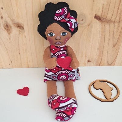 Boneca de pano com vestido estampado rosa e branco segurando coração vermelho